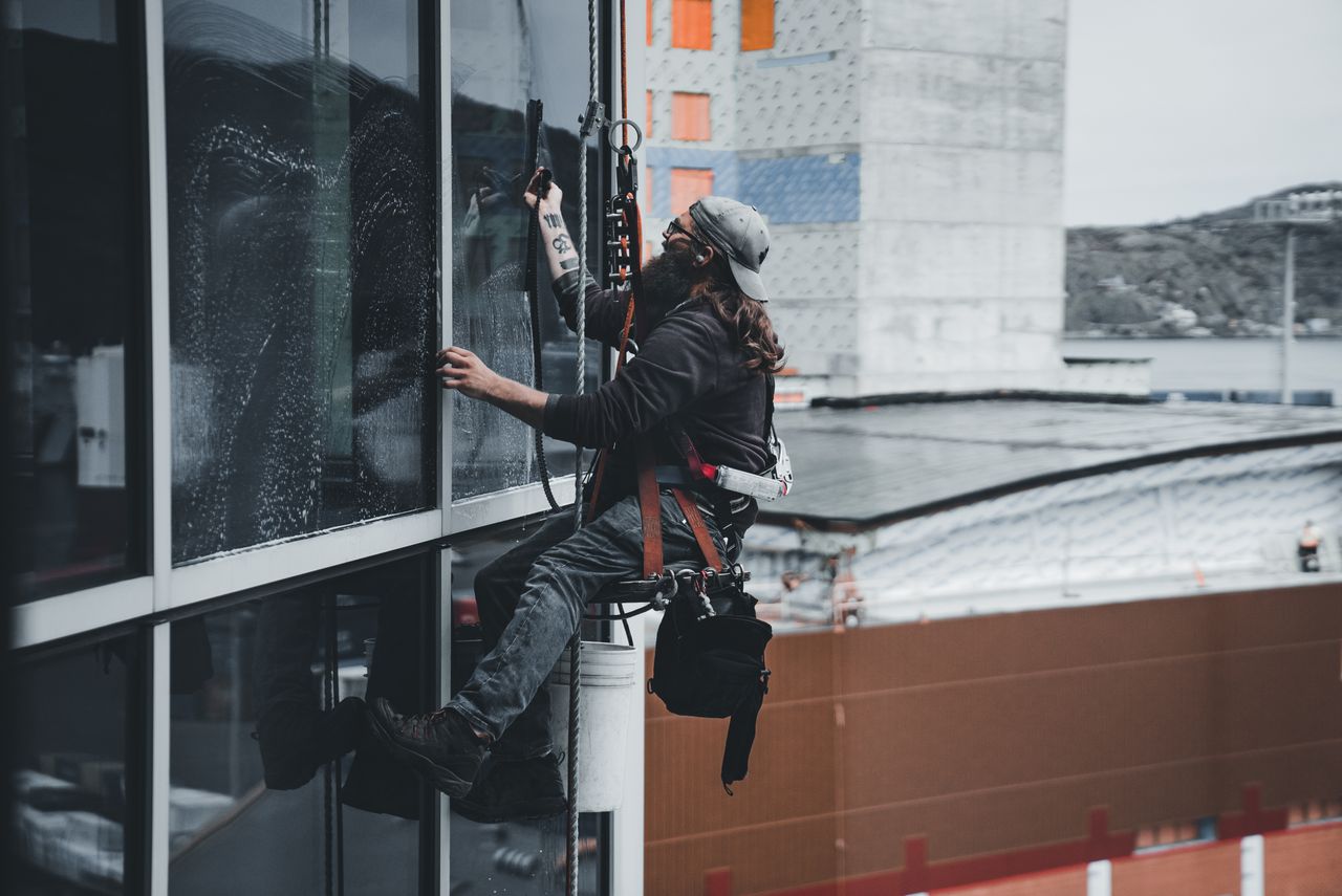 about-01 A man cleaning skyscraper windows with a harness, showcasing urban high-rise work.